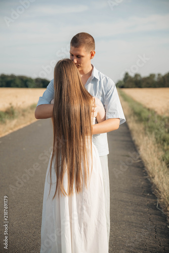 Obraz na plátně Young couple embracing on a rural road surrounded by fields, seen from behind