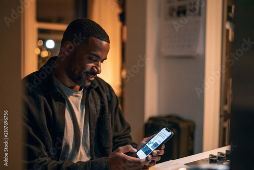 Young black man using smartphone and smiling in a cozy indoor setting  