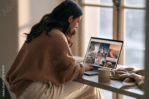 Young woman working on a laptop at a sunlit table with coffee  