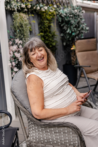 Картината върху платно older woman laughing happily while relaxing in a garden chair in summer