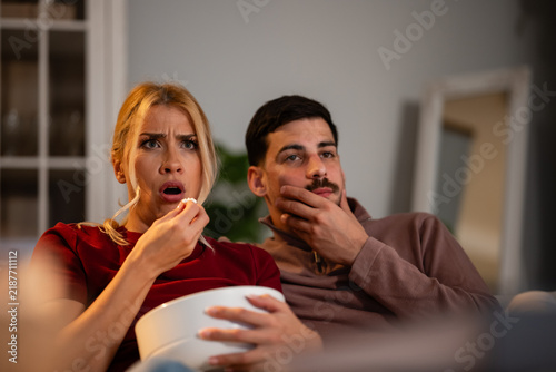 фотографія Couple watching thrilling movie at home, reacting to suspense