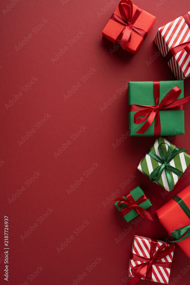 Naklejka premium Stack of red and green Christmas presents with ribbons and striped wrapping on vertical maroon red background