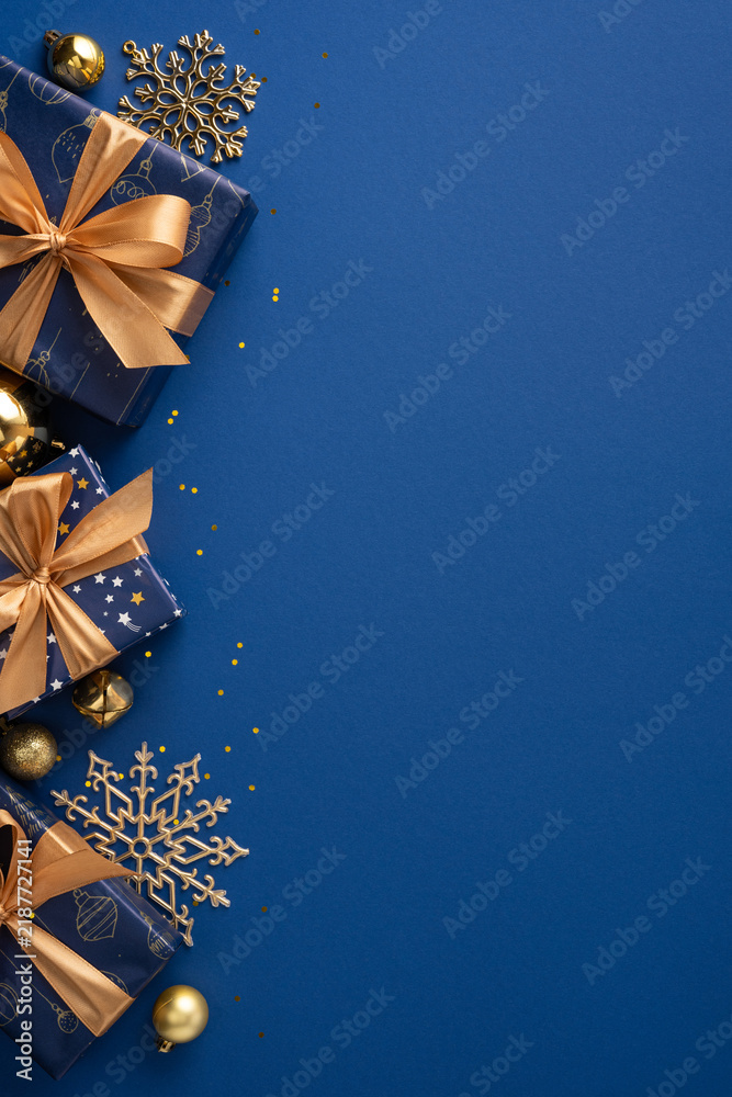 Obraz premium Merry Christmas and Happy New Year blue and gold presents with ribbon and snowflake decorations on dark blue backdrop with space for greetings