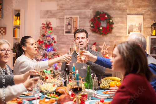 Принти на полотні Family members clink glasses over a festive dinner table, capturing a joyful Christmas toast, togetherness and shared celebration with seasonal food and decorations in a warm holiday home