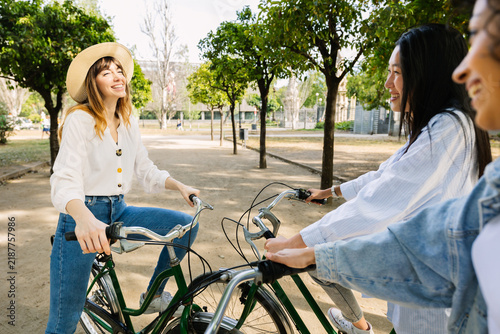 Young group of multiracial women friends chatting closely by a bicycle together outdoors in the city. Friendship and travel concept.