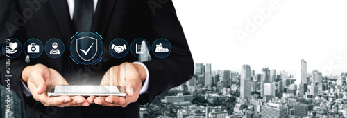 Businessman in Suit Holding Smartphone with Digital Icons of Security  Technology  and Connectivity Over Cityscape Background. Glyphic.