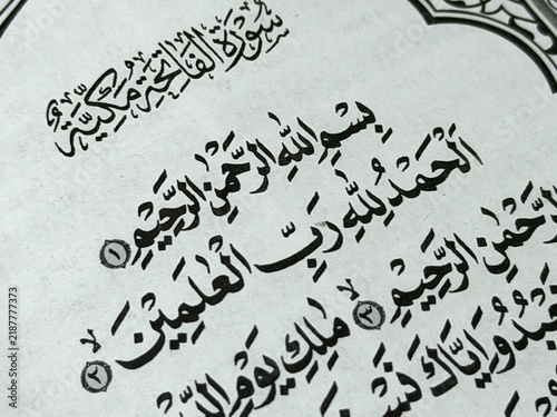 Close up photo of Al Fatihah verse, Alhamdulillahi Robbil Alamiin calligraphy text on Quran page background