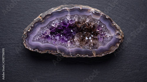 Geode slice with crystal interior displaying purple agate bands and sparkling mineral texture on dark surface
