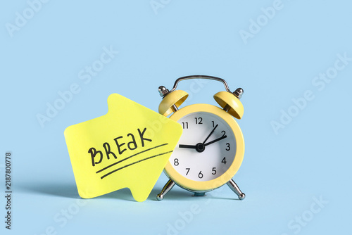 Quadro su tela Alarm clock with word BREAK on paper arrow against blue background