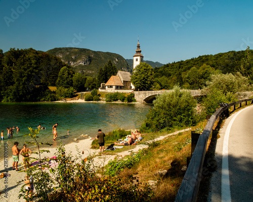 фотографія Tourists relax and swim on the sunny banks of Lake Bohinj, Slovenia, with the iconic Church of St