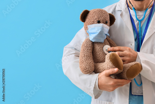 Male pediatrician with stethoscope listening to toy bear on blue background