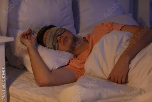 Handsome young man with mask sleeping on bed in evening at home
