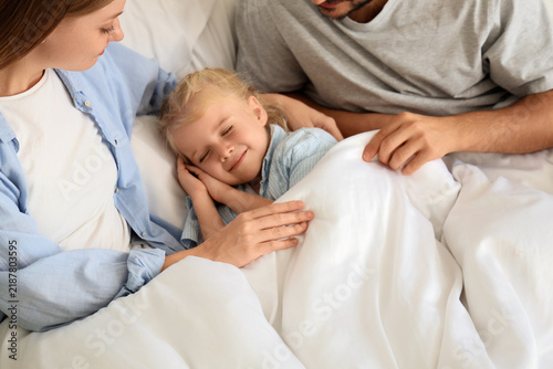 Cute little girl sleeping with her parents under blanket in bedroom