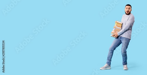 Academic overload and student stress, young man carrying a heavy stack of boo...