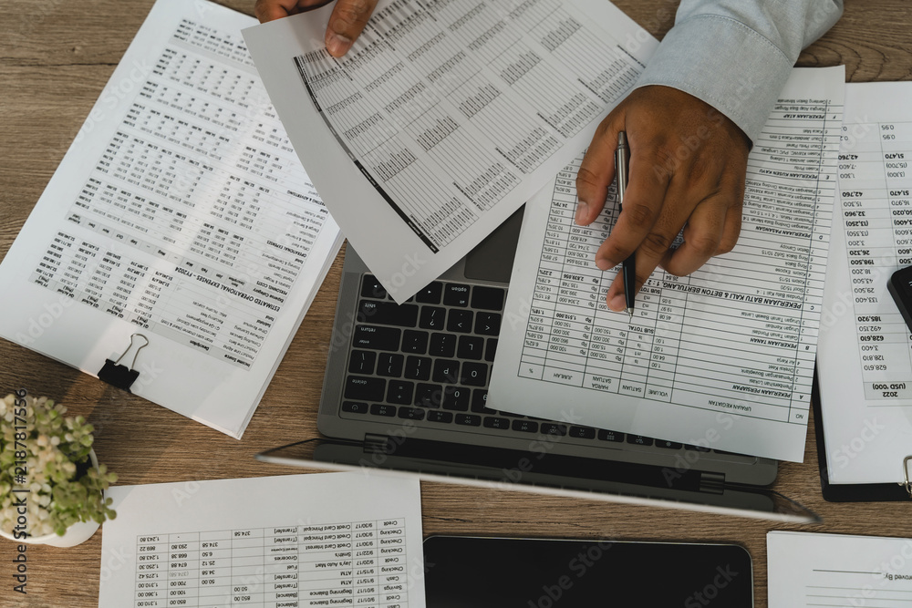 Obraz premium Businessman top view printed financial reports over laptop, checking accounting figures and business records for financial report review and data analysis.