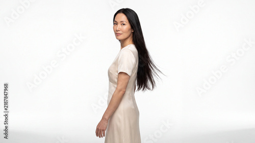 Asian woman with long straight black hair turns around slightly while posing against a clean white studio background.