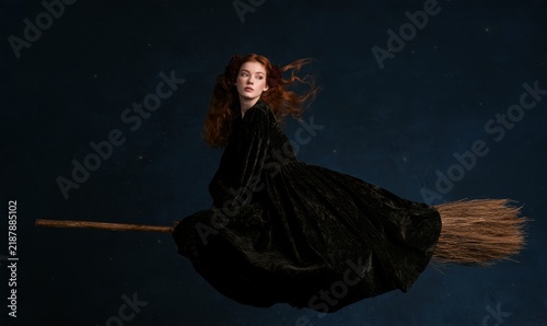 Girl dressed in black cloak rides wooden broomstick through night sky