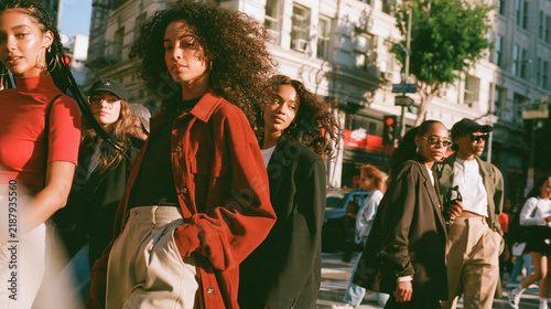 Urban Style Ensemble: A group of stylish young individuals, exuding urban chic, stride confidently across a sun-drenched city street, a vibrant tapestry of modern fashion and metropolitan life.