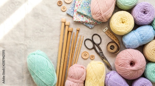 Knitting supplies flat lay with colorful pastel yarn and wooden needles on linen background.