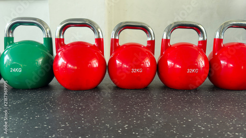 Green 24 kg and red 32 kg kettlebells with polished metal handles arranged in a row on a rubber floor, illustrating progressive strength, weight choice, functional fitness, and gym training.