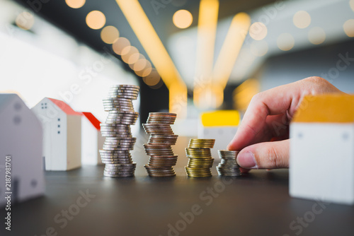 Konstfotografi Real estate and property investment concept with hand stacking coins beside miniature house models on table for housing savings, mortgage home loan down payment and financial growth
