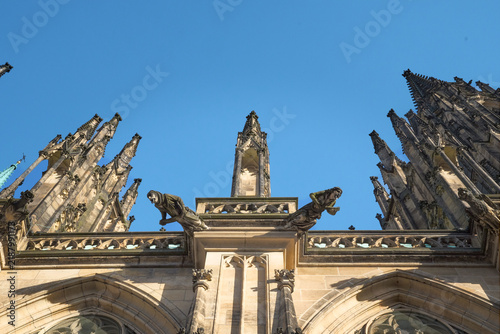 Low-angle close-up of stone gargoyles and intricate Gothic pinnacles on St. Vitus Cathedral in Prague Castle, Czech Republic.