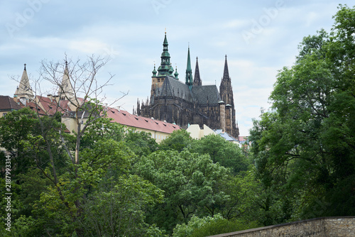 Side profile view of St. Vitus Cathedral rising above lush green trees in Prague Castle, Czech Republic.