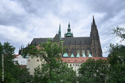 Side profile view of St. Vitus Cathedral rising above lush green trees in Prague Castle, Czech Republic.