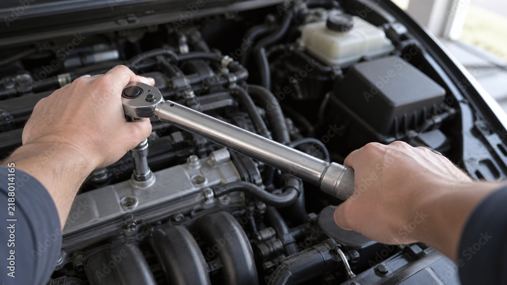 Fototapeta premium Auto mechanic using a torque wrench to tighten bolts on a car engine bay