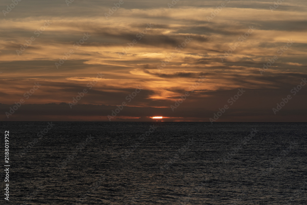 Fototapeta premium オレンジ色のグラデーションの空と水平線に太陽が沈む寸前の海