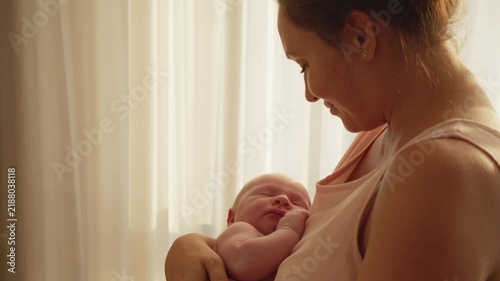 Happy mother holds a baby in her arms at sunset. A cute infant sleeps in his mother's arms. Concept of happy parenthood. Mother is rocking her newborn son in her arms. Mother and child.