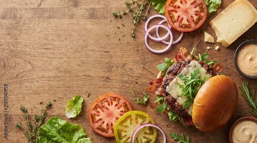 Gourmet Bacon Cheeseburger and Fresh Ingredients on Rustic Wooden Table with Copy Space