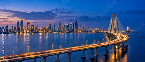 Mumbai skyline at dusk with illuminated Bandra-Worli Sea Link bridge, city lights reflecting on water, modern Indian metropolis cityscape.