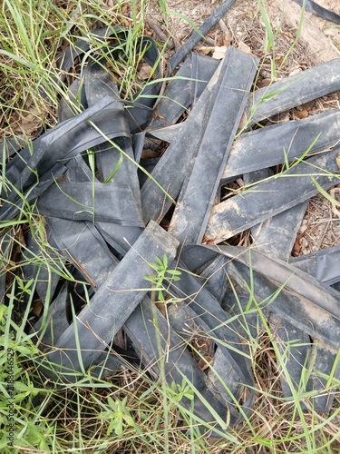 Bild auf Leinwand Discarded Black Rubber Straps And Debris Tangled In Green Grass Field Outdoors