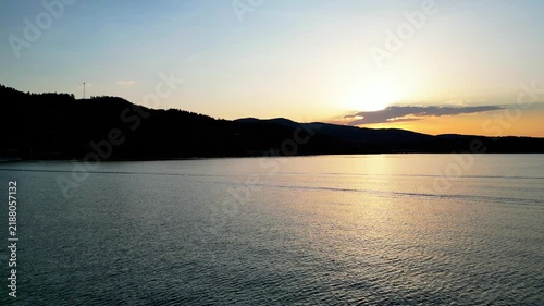 Beautiful drone footage of Lake Mucharskie during sunset, featuring warm golden reflections on steel-blue water and dark Beskid mountains against a colorful sky.