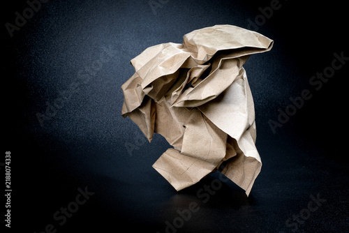 Картината върху платно Close-up of a crumpled brown kraft paper ball resting on a dark surface under dramatic spotlight symbolizing a rejected creative idea