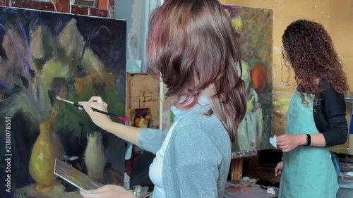 Teenage girl in college painting class, art studio, art workshop. She paints still life on canvas with oil paints. 
