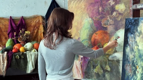Teenage female artist in college painting class, art studio, art workshop. She paints still life on canvas with oil paints. 