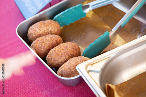 Foto Breaded fried croquettes in metal serving tray with turquoise tongs on bright pi