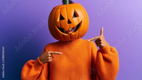 Person wears pumpkin mask, orange sweater