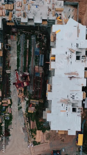 Aerial drone view of a new residential building under construction, showing concrete structures, construction equipment and urban development from above.
