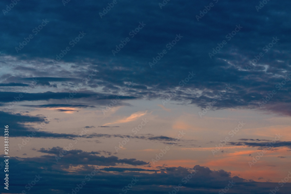 Obraz premium Golden sunlight breaking through dark dramatic storm clouds at sunset, creating a moody atmospheric sky background with glowing sun rays.
