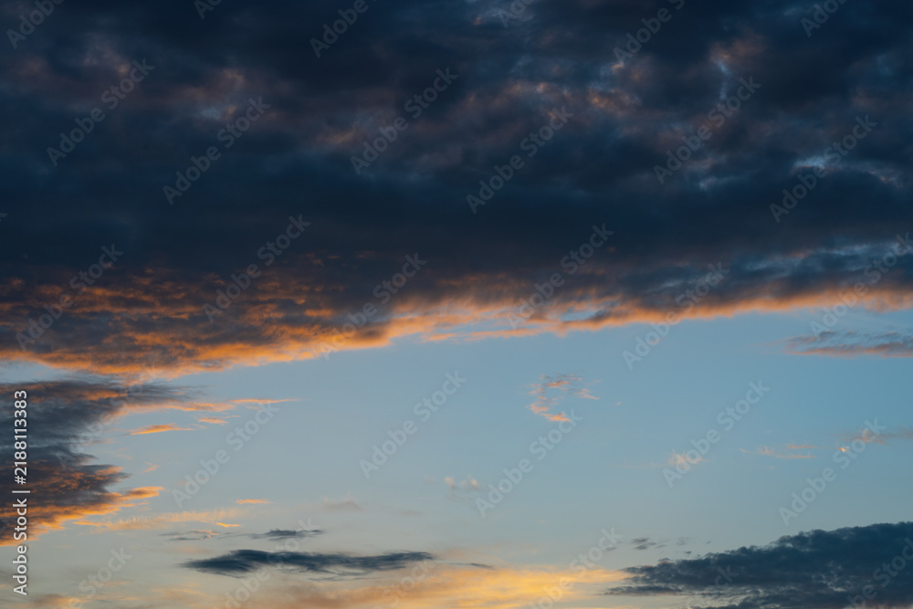 Fototapeta premium Golden sunlight breaking through dark dramatic storm clouds at sunset, creating a moody atmospheric sky background with glowing sun rays.