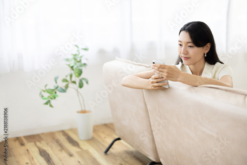 Young Japanese woman using a smartphone on a sofa by a bright window