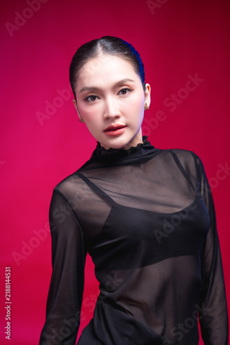 Quadro su tela A captivating beauty portrait with the head tilted, direct gaze meeting the camera, elegant neckline and sleek updo against a deep red backdrop, blending allure with poise