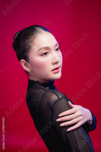Quadro su tela A captivating beauty portrait with the head tilted, direct gaze meeting the camera, elegant neckline and sleek updo against a deep red backdrop, blending allure with poise