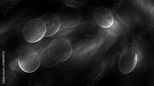 Blurred circular bokeh lights. Abstract black and white background. Monochrome defocused glowing flares and smoky texture overlay.