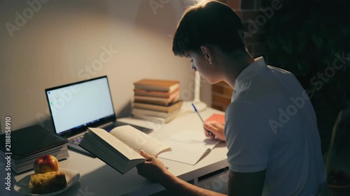 Dedicated youth reading literature at the illuminated home desk.