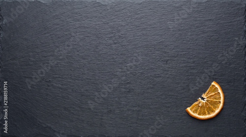 A Single Dried Orange Slice Placed Elegantly on a Dark Slate Background, Highlighting Natural Textures and Colors in Culinary Presentation