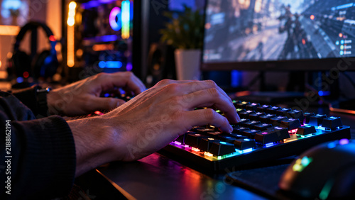 Close-up of a gamer using a mechanical RGB keyboard and gaming mouse in a dark computer setup with a high-performance gaming monitor